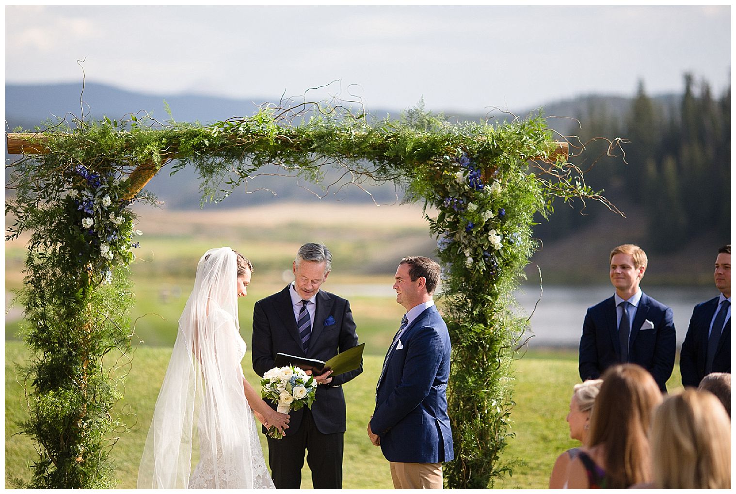 新郎新婦は、キーストーン牧場の結婚式場で花で飾られた祭壇の下に立っています。