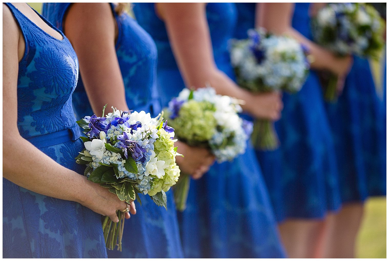 Brautjungfern halten ihre blauen, weißen und grünen Blumensträuße während einer Keystone Mountain-Hochzeit gegen ihre blauen Kleider.