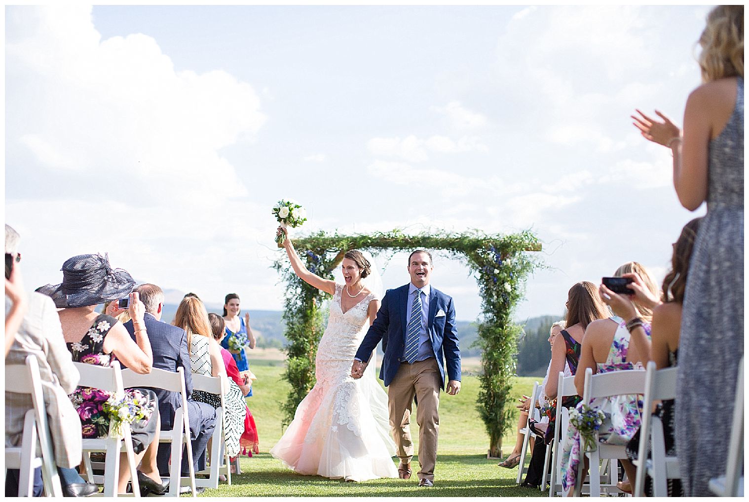 a noiva segura seu buquê alto enquanto ela e seu noivo caminham felizes de volta ao corredor juntos no local da cerimônia do local do casamento de Keystone Ranch.