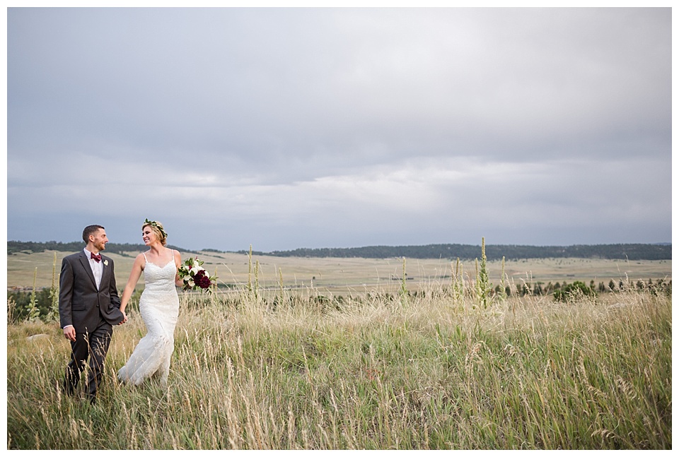 bride and groom walking through a meadow at sunset at spruce mountain ranch