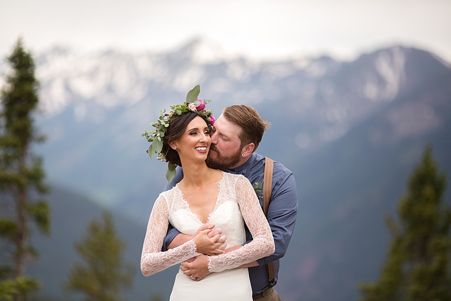 groom kisses and hugs bride from behind at the top of the mountain in aspen colorado 