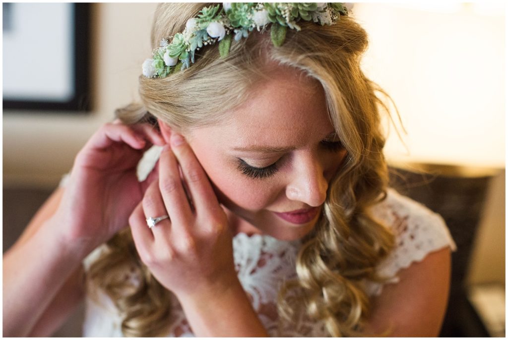bride with succulent flower crown putting earrings in on her wedding day