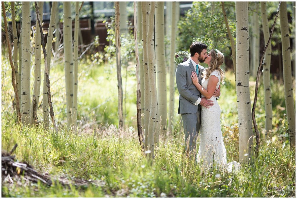 wedding couple share a kiss during bridal portraits surrounded by aspen trees and greenery
