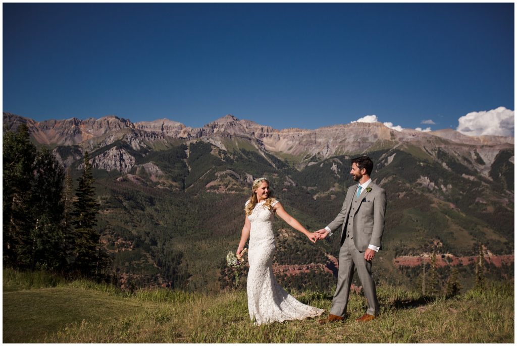 bride holds groom's hand and looks back at him with gorgeous Telluride mountains in backdrop 