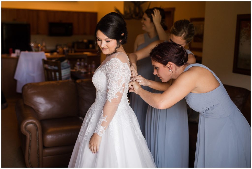 bridesmaid best friend helping bride put on her long sleeved wedding dress designed by Allure