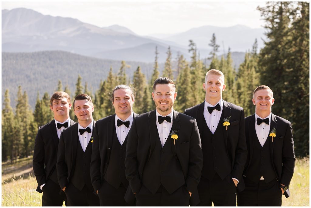 groom poses with his groomsmen wearing black tuxes with black ties and sunflowers