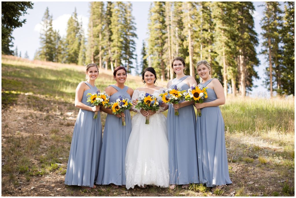 bride poses with her bridesmaids wearing blue dresses and holding sunflowers in keystone Colorado 