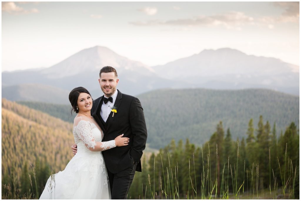 bride poses with her hand on groom's chest in front of stunning Colorado mountain backdrop