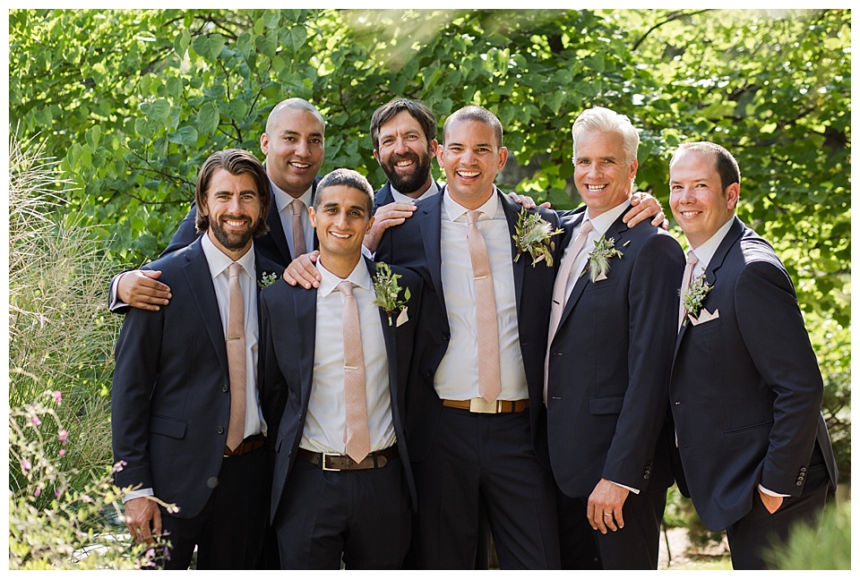 groom poses with his groomsmen in the greenery at denver botanical gardens