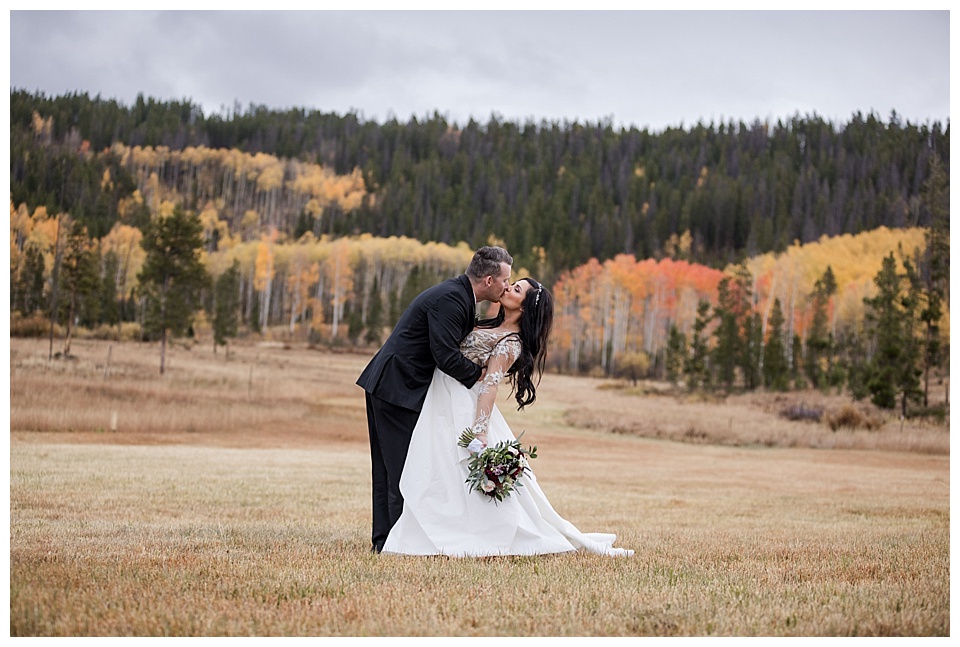 groom dips kiss bride with beautiful fall foliage at devil's thumb ranch