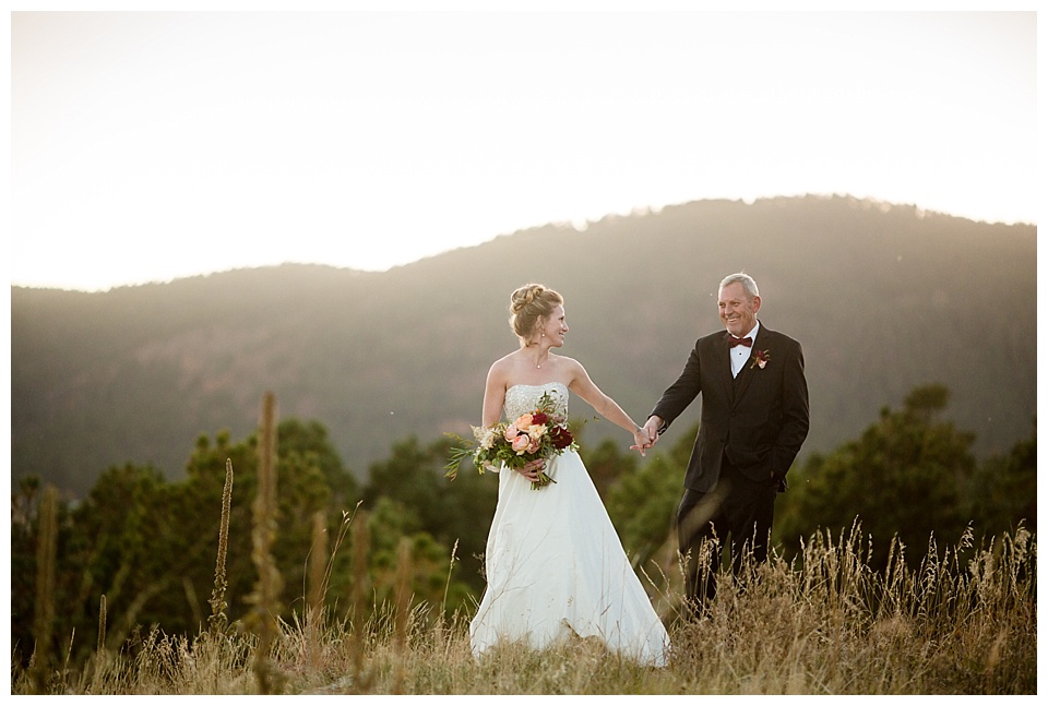 bride holds groom's hand with stunning mountain sunset at spruce mountain ranch