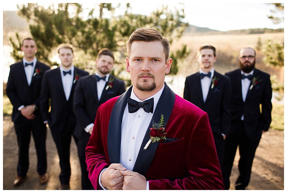 groom wearing red velvet suit and groomsmen pose with serious faces at spruce mountain ranch