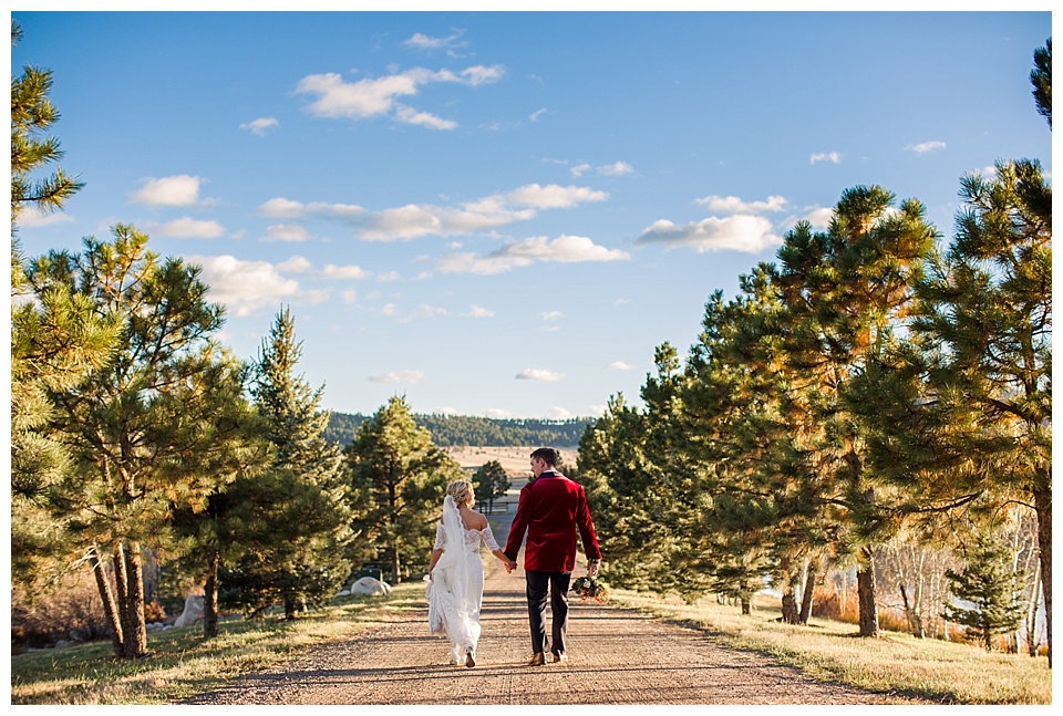 bride and groom walking along dirt road with perfect blue sky at spruce mountain ranch