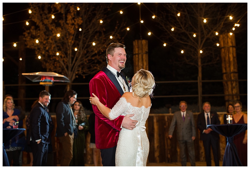 groom wearing red velvet suit jacket laughing during first dance with his wife