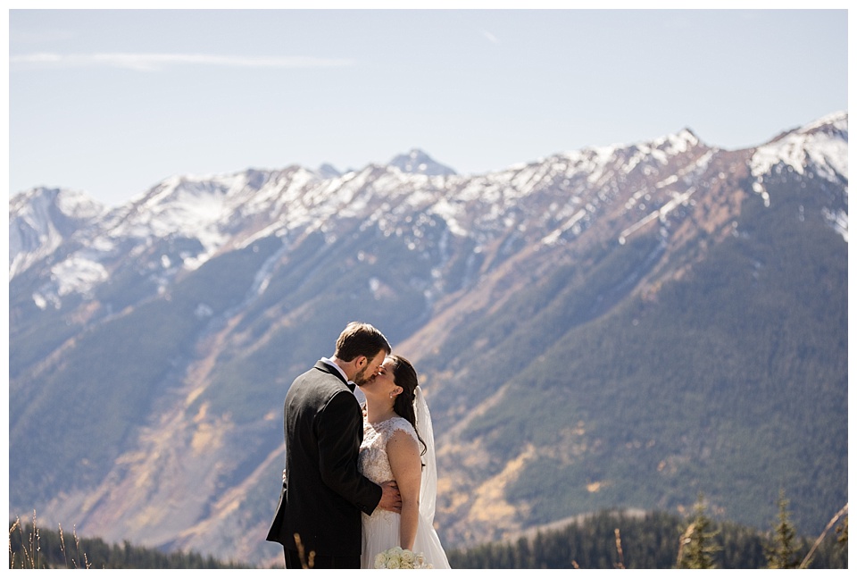 bride and groom kiss with stunning mountain backdrop