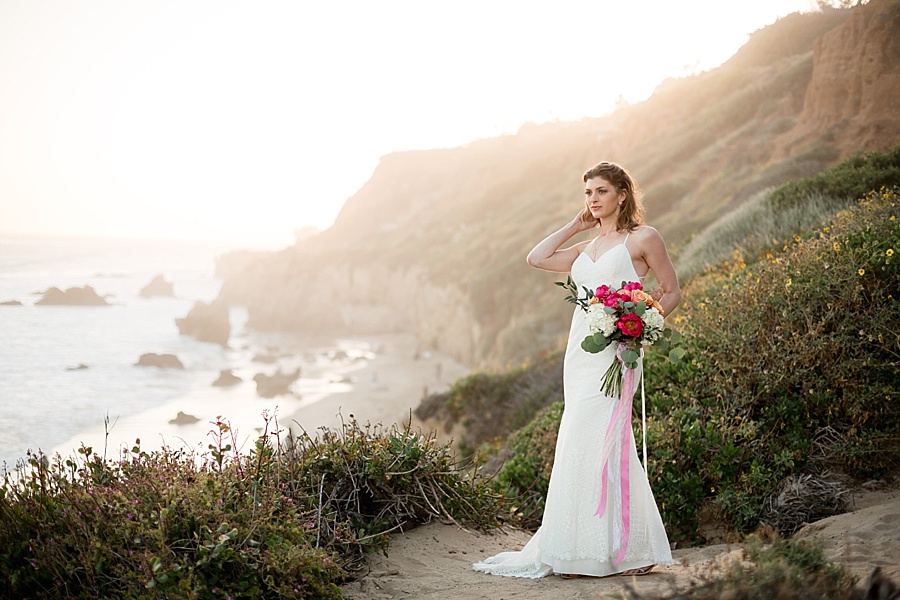 bride poses on sea cliff at sunset at matador beach