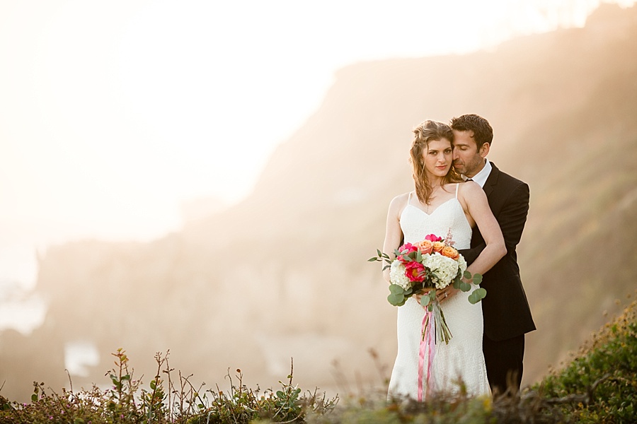 groom holds bride from behind with srunning sea cliff background at matador beach