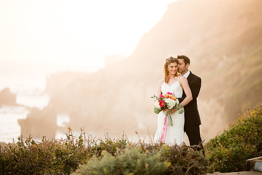groom holds bride from behind with srunning sea cliff background at matador beach