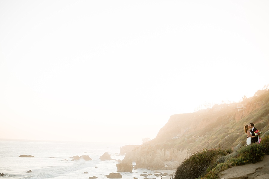 wedding couple pose in front of stunning sea cliff sunset at matador beach