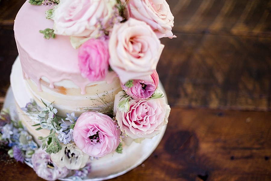 pink icing dripping on wedding cake with pink pastel flowers 