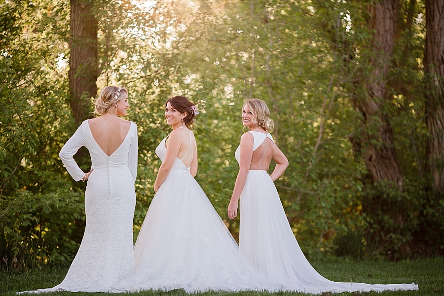three brides pose showing off the backs of their wedding dresses
