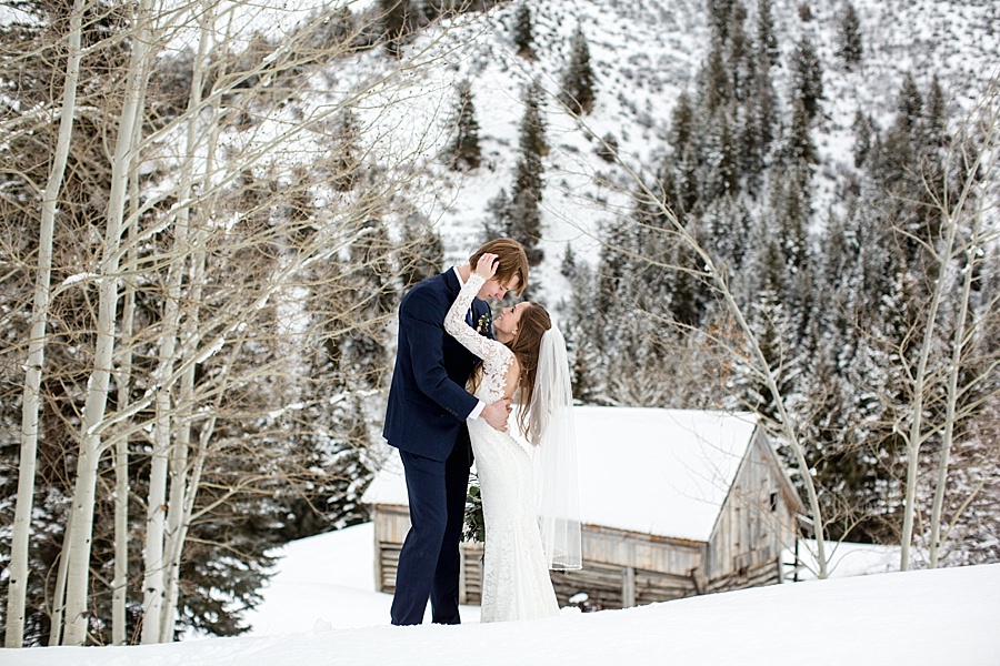 bride holds groom's face in the snow in front of a snowy cabin in beaver creek