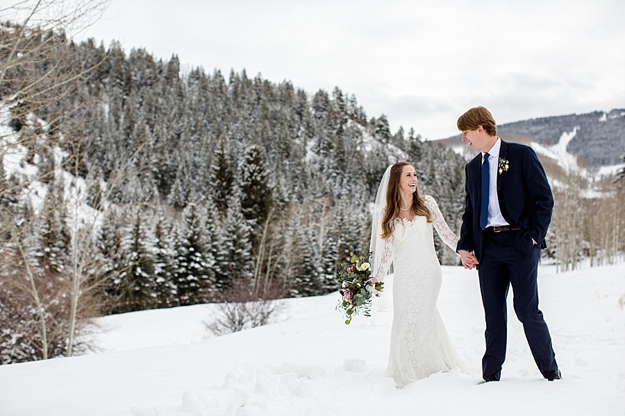 bride and groom walking in the snow with colorado mountains in the background