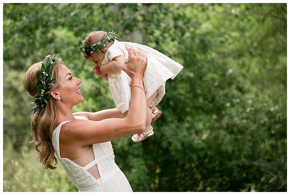 bride holds her baby flower girl in the air on her wedding day in the Colorado mountains 