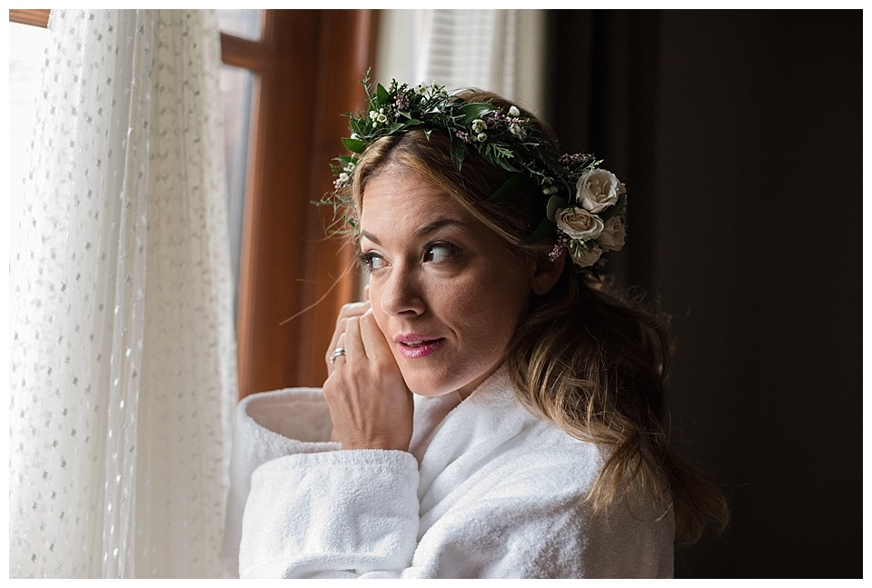 bride putting her earrings in while wearing a flower crown and a white robe
