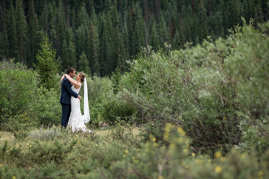 bride holds groom's neck in the lush colorado mountains 