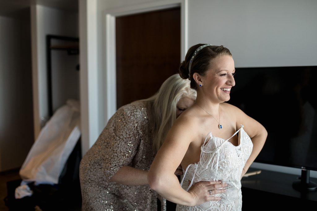 bride with hands on hips as her mother helps her put on her wedding dress