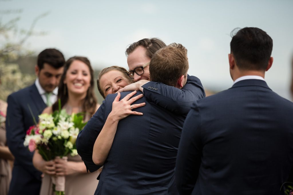 bride and groom hug friend who did a reading at their wedding ceremony 