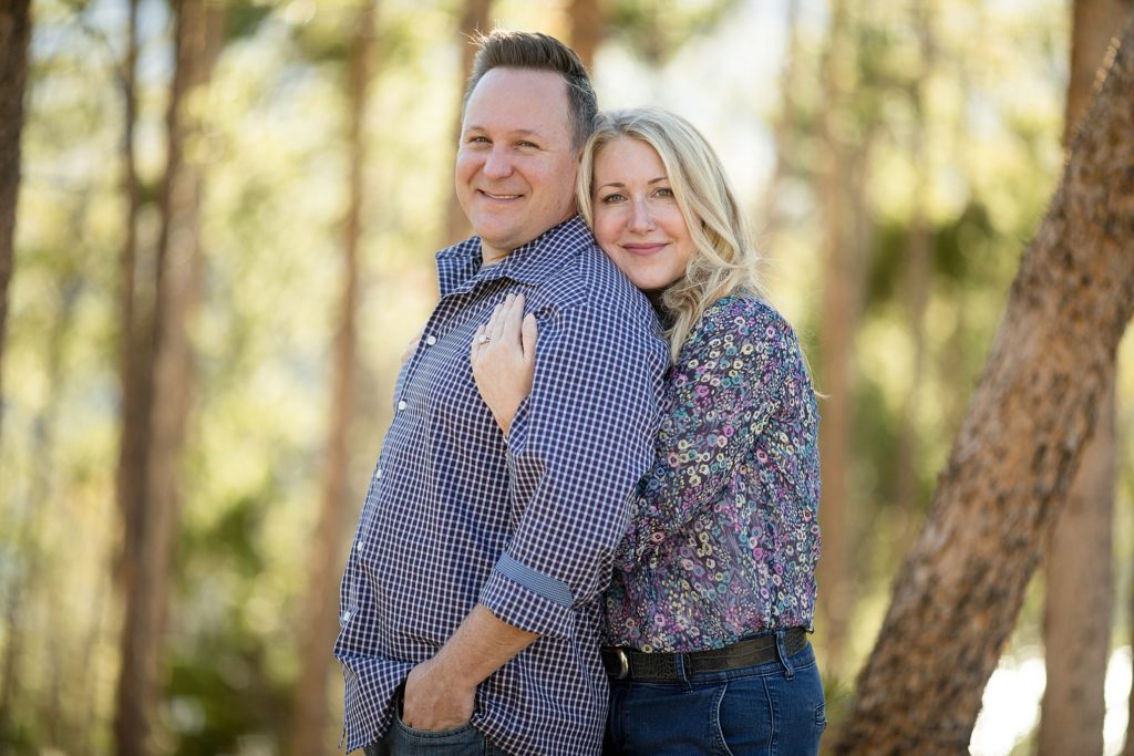 bride hugs groom from behind during engagement session in the mountains