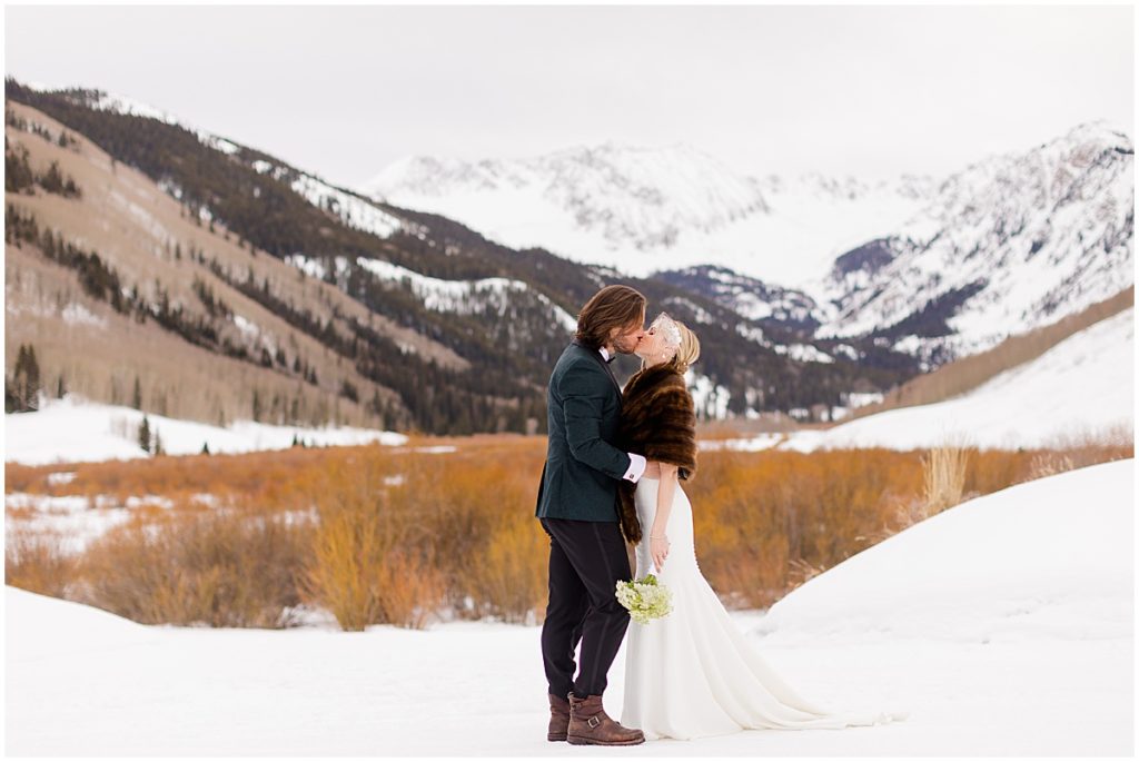 Bride and groom outside at The Pine Creek Cookhouse in the winter snow.  The bride is wearing a dress from Jenny Yoo holding bouquet designed by Aspen Branch Design.