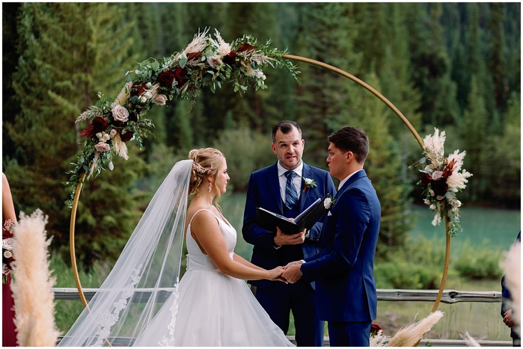 Bride and groom during wedding ceremony at Ski Tip Lodge.  Floral arch decorated by Pots and Petals Floral Design
