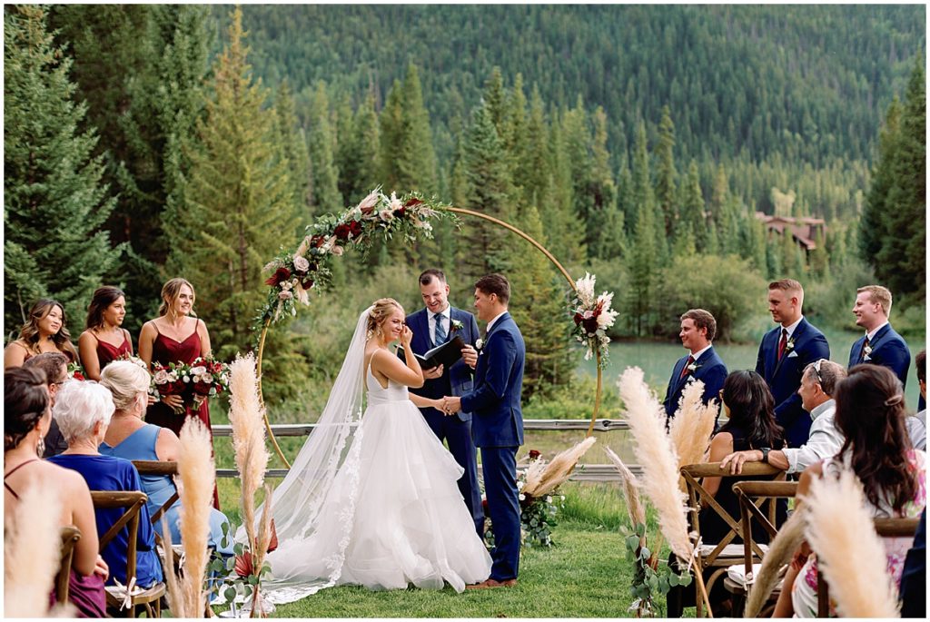 Bride and groom during wedding ceremony at Ski Tip Lodge.  Floral arch decorated by Pots and Petals Floral Design