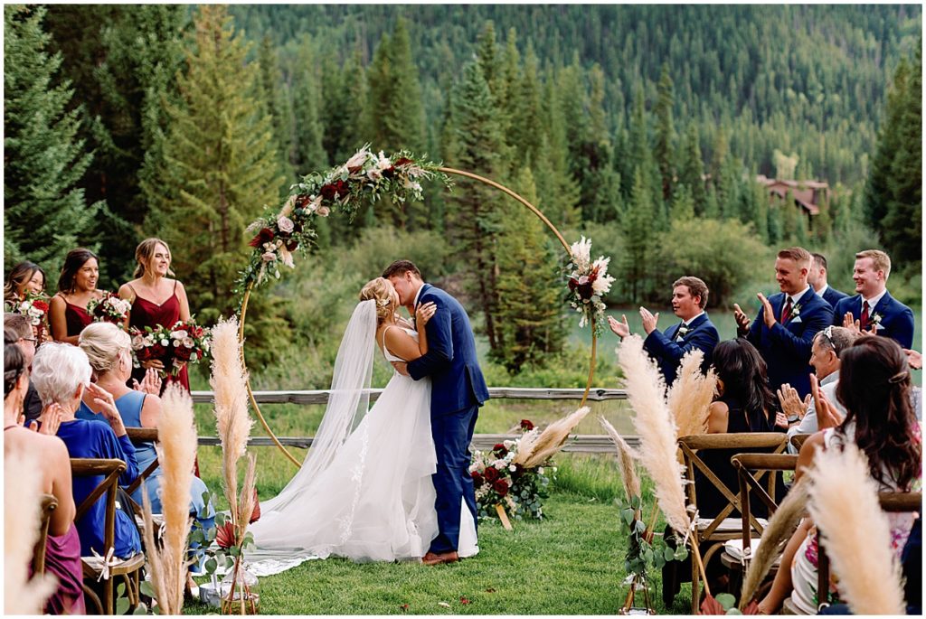 Bride and groom kiss during wedding ceremony at Ski Tip Lodge.  Floral arch decorated by Pots and Petals Floral Design