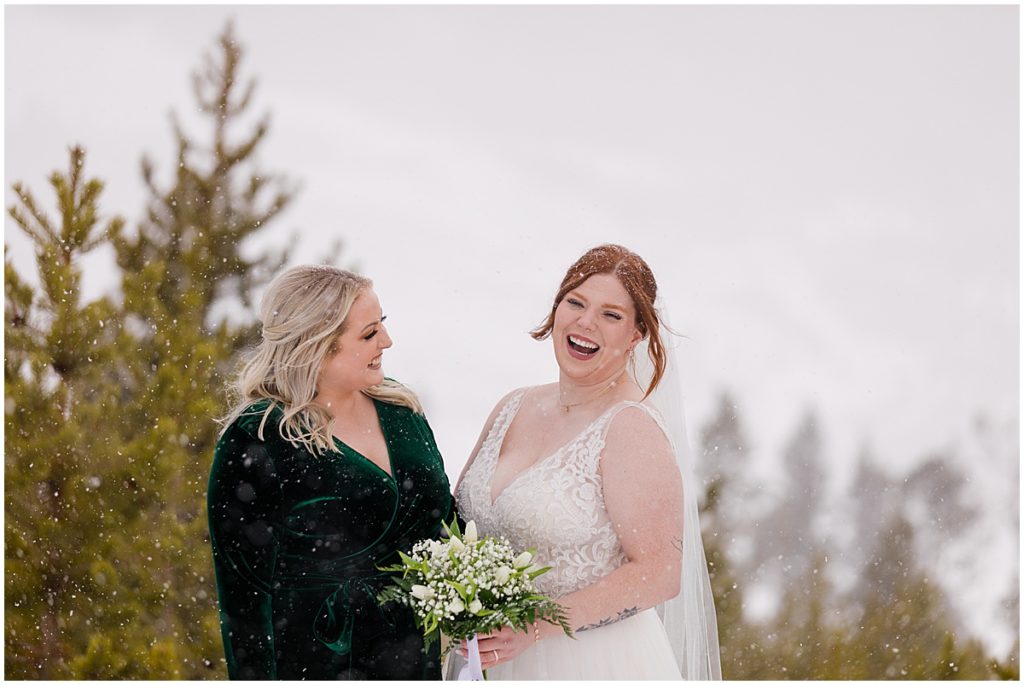 Bride and bridesmaid at Sapphire Point in Breckenridge for a micro wedding ceremony.  Bride is wearing a dress from Champagne and Lace Bridal.  Bride is holding a bouquet designed by Garden of Eden Flowers and Gifts.