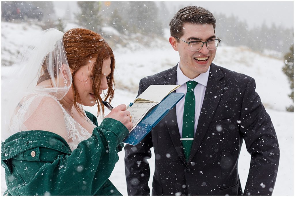 Bride and groom signing marriage license at Sapphire Point in Breckenridge during winter micro wedding ceremony.  Bride is wearing a dress from Champagne and Lace Bridal.  Bride is holding bouquet designed by Garden of Eden Flowers and Gifts.