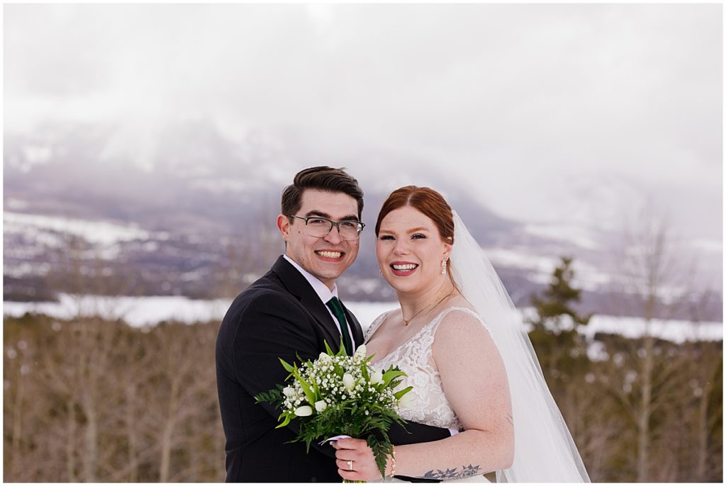 Bride and groom at Sapphire Point in Breckenridge during winter micro wedding ceremony.  Bride is wearing a dress from Champagne and Lace Bridal.  Bride is holding bouquet designed by Garden of Eden Flowers and Gifts.