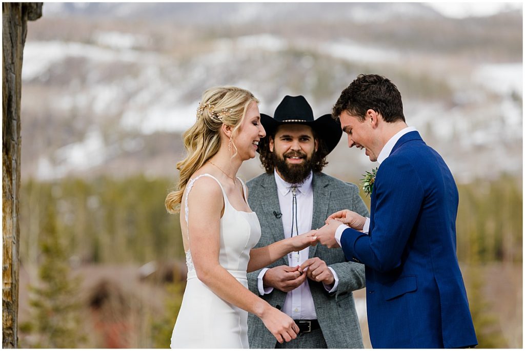 Groom putting ring on bride's finger during ceremony at Devil's Thumb Ranch.