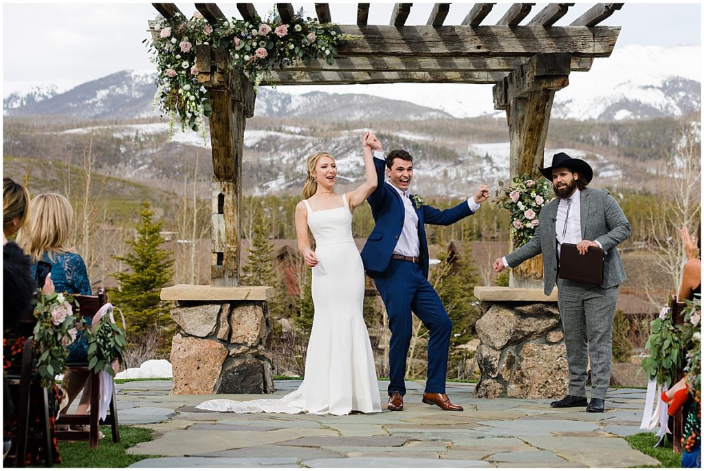 Bride and groom hold hands in the air celebrating being newlyweds at Devil's Thumb Ranch.