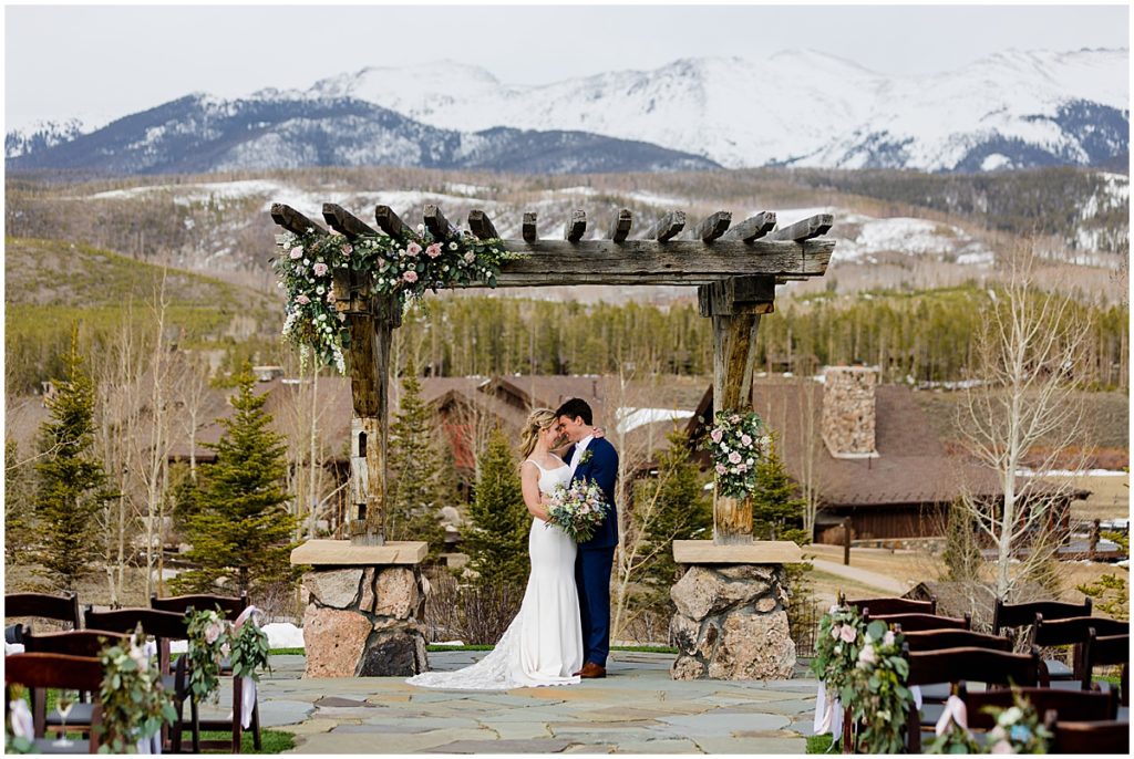 Bride and groom under alter with snowy mountain tops after wedding ceremony at Devil's Thumb Ranch