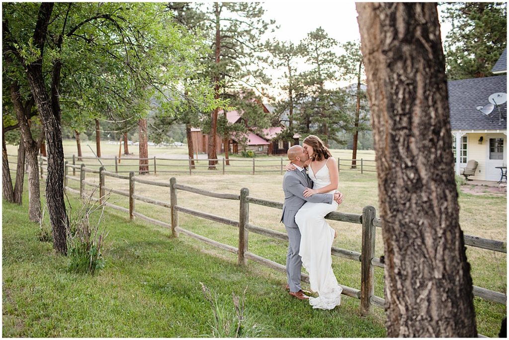 Bride sitting on fence hugging and kissing groom outside after elopement at Three Sisters Park in Evergreen