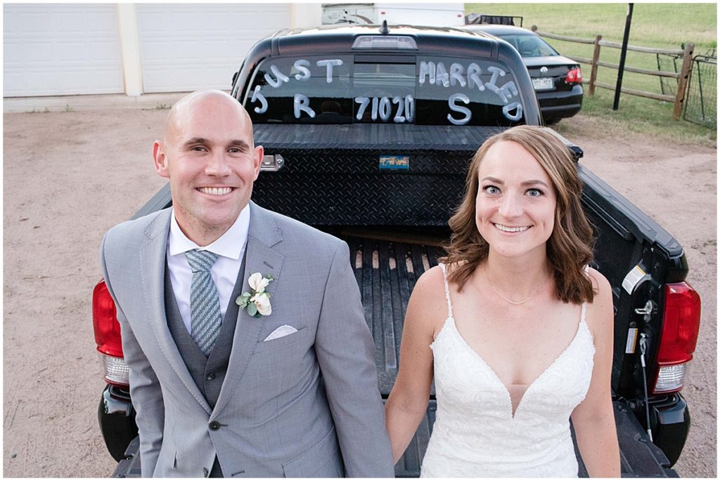 Bride and groom sitting on pickup truck bed with just married written on the window at Three Sisters Park in Evergreen
