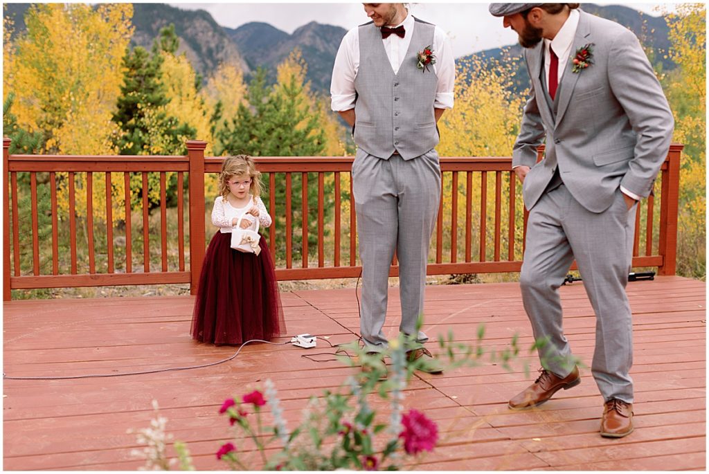 Groom and officiant watching Flower girl spreading petals on patio for wedding at Frisco Day Lodge