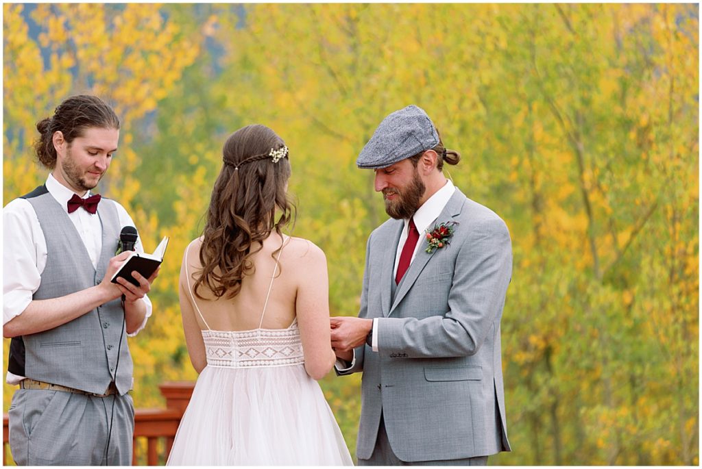 Groom putting ring on bride's wedding finger during ceremony at Frisco Day Lodge