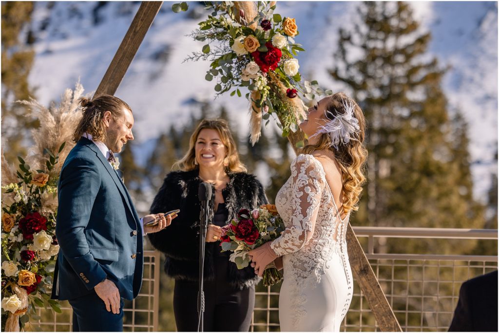 Bride and groom laughing during wedding ceremony outside at Arapahoe Basin.  Floral decor by Plum Sage Flowers.
