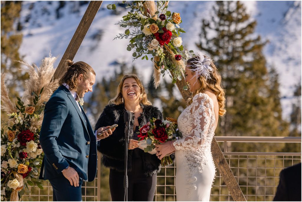 Bride and groom laughing during wedding ceremony outside at Arapahoe Basin.  Floral decor by Plum Sage Flowers.