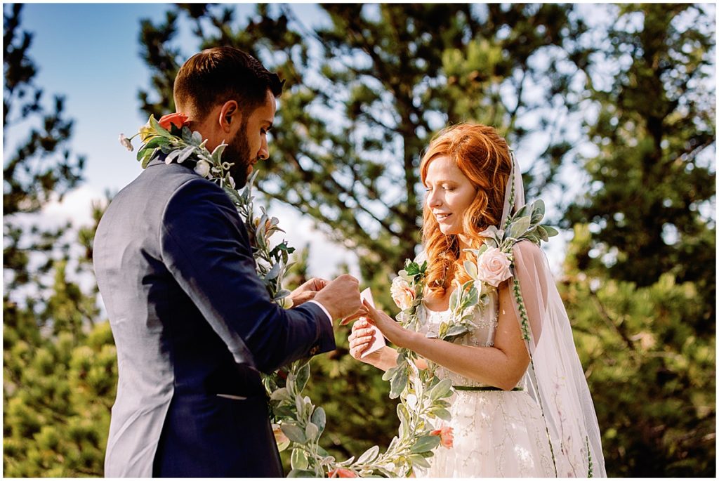 Exchanging rings during elopement ceremony at Blue Sky Mountain Ranch in Blackhawk with bride wearing dress from BHLDN and designed by Watters.  Groom is wearing suit from Indochino.  Floral design by Blush & Bay.